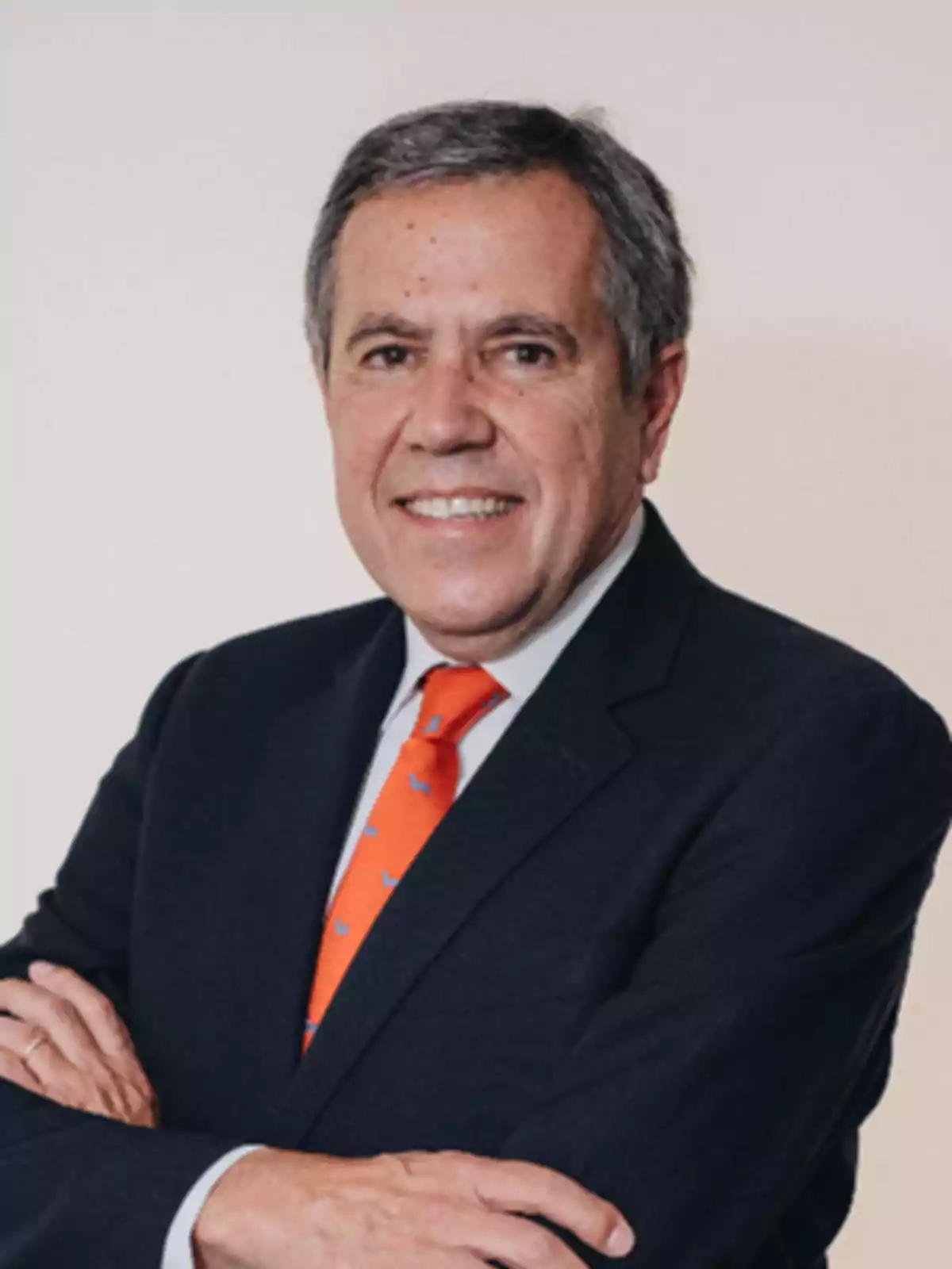 Hombre de mediana edad con traje oscuro y corbata naranja sonriendo con los brazos cruzados.