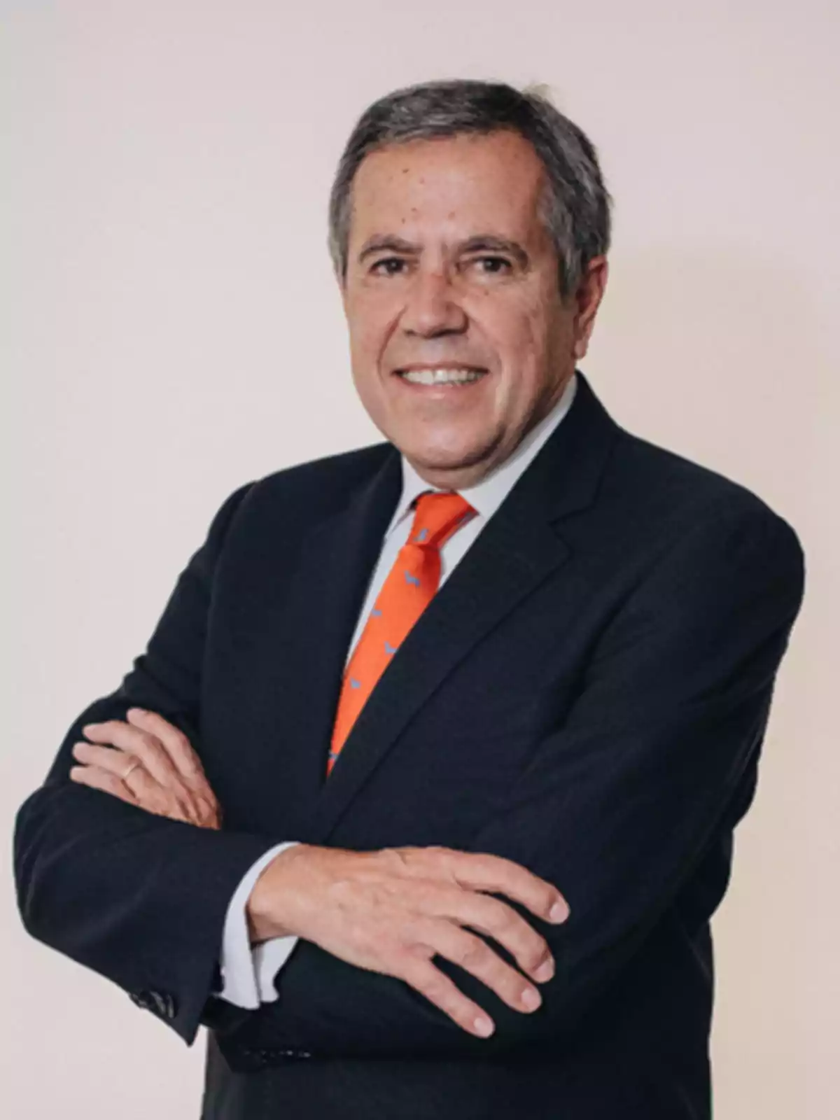 Hombre de mediana edad con traje oscuro y corbata naranja, sonriendo con los brazos cruzados.