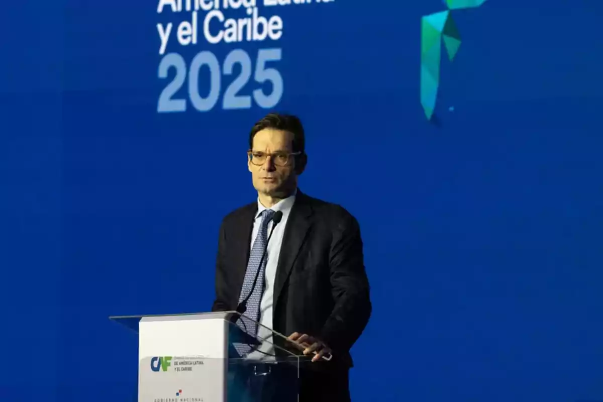 Hombre con gafas y traje hablando en un podio durante un evento con fondo azul que muestra el texto América Latina y el Caribe 2025 Hombre con gafas y traje hablando en un podio durante un evento con fondo azul que muestra el texto América Latina y el Caribe 2025