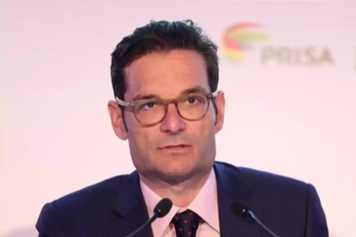 Un hombre con gafas y traje oscuro hablando frente a un micrófono.