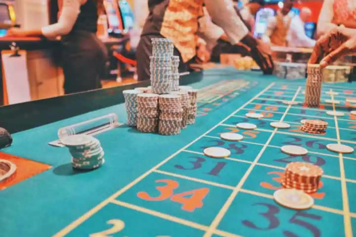 Mesa de ruleta en un casino con fichas apiladas y personas jugando.