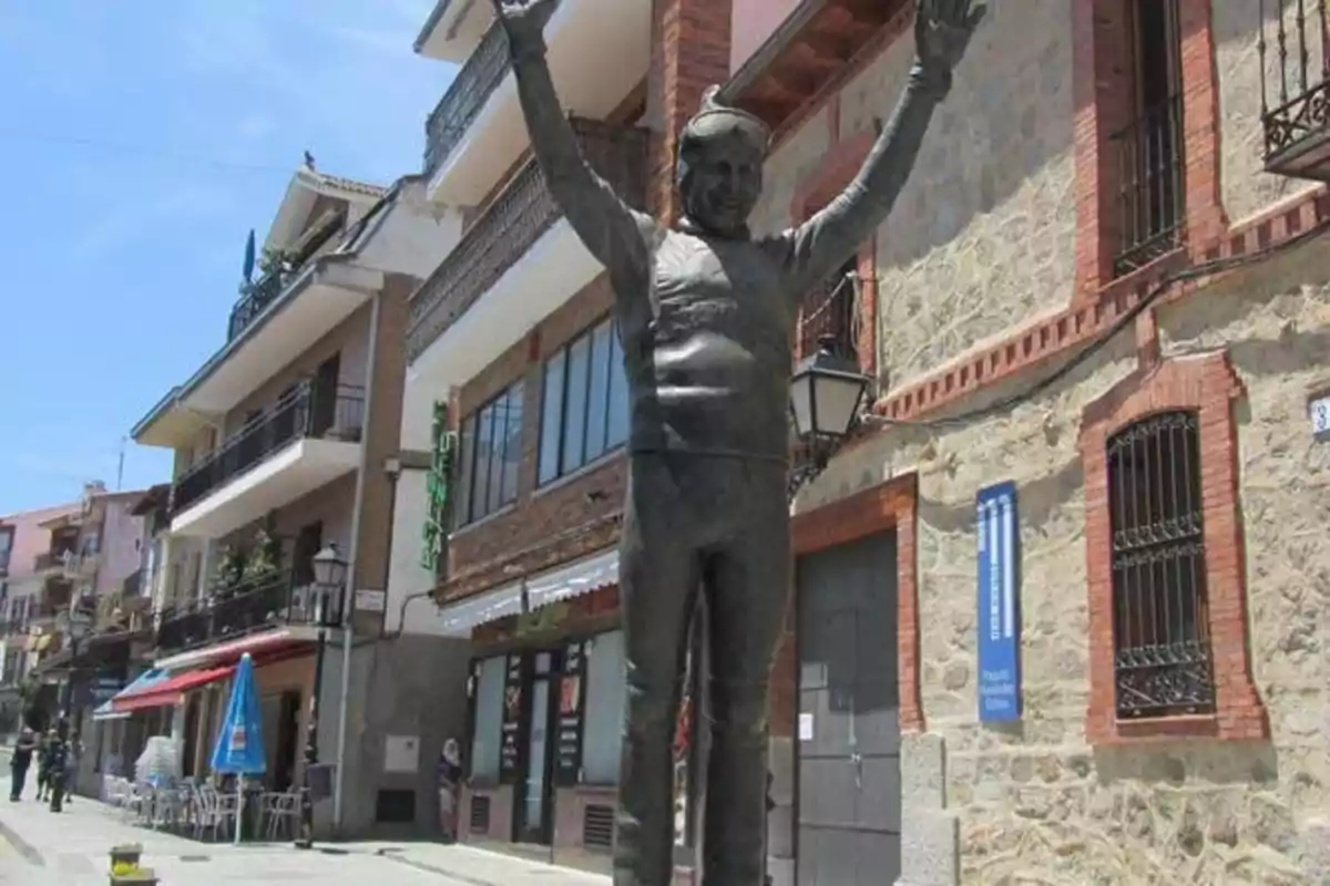 Estatua de un hombre con los brazos levantados en una calle con edificios y tiendas.