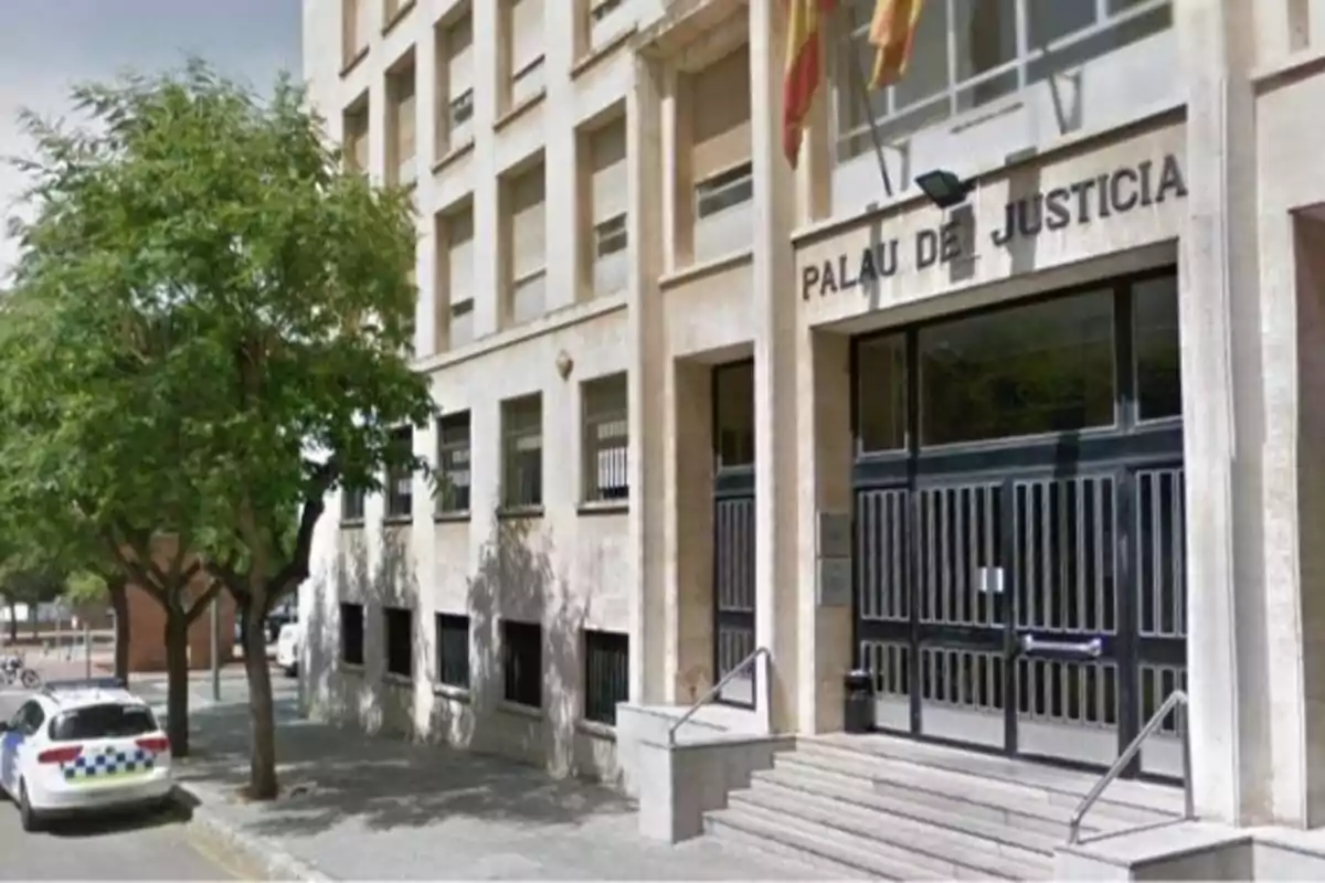 Edificio del Palau de Justicia con una entrada principal y una patrulla de policía estacionada en la calle.