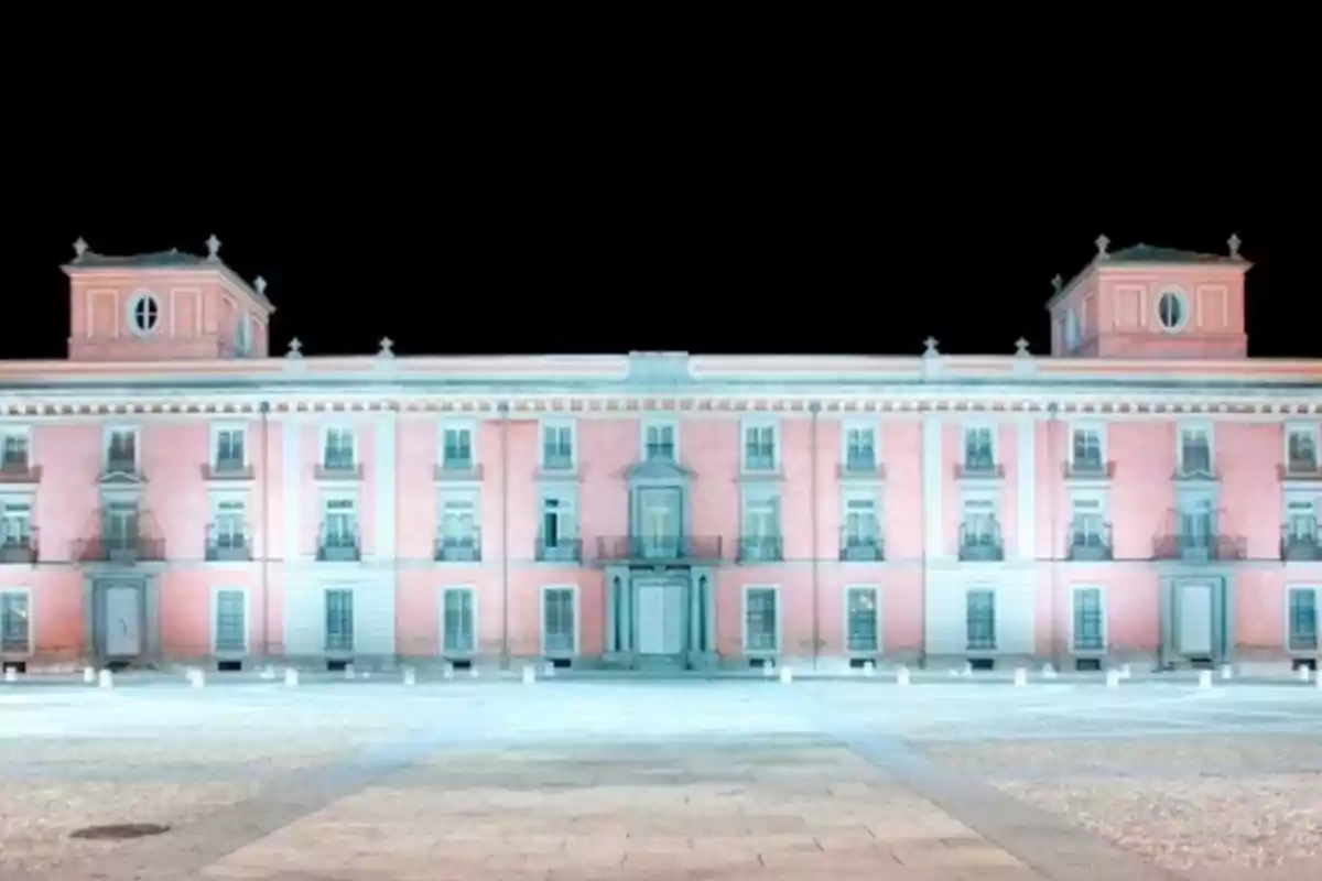 Edificio histórico de fachada rosa iluminado por la noche con cielo negro de fondo.