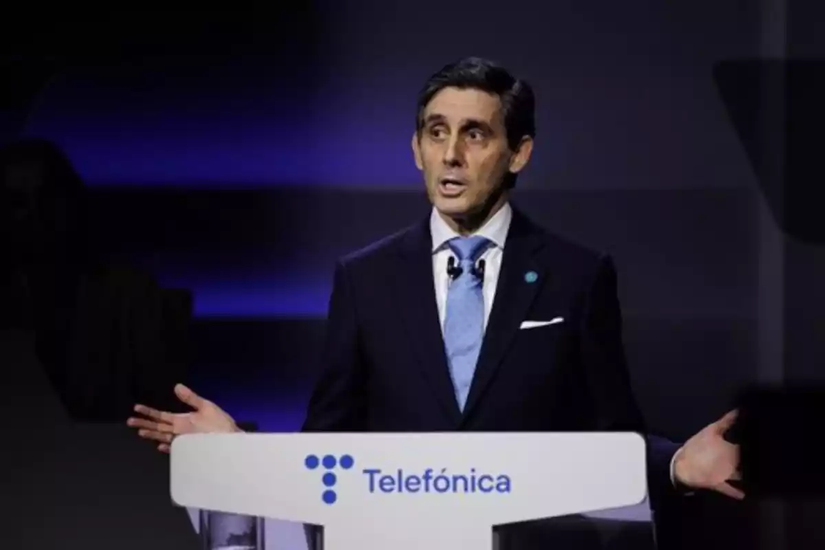 Un hombre en traje oscuro y corbata azul habla desde un podio con el logo de Telefónica en un escenario iluminado en tonos azules.