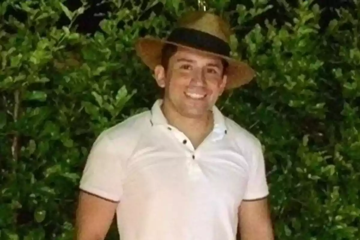 Hombre con sombrero de paja y camisa blanca sonriendo frente a un fondo de vegetación.