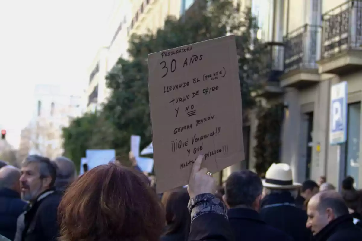 Una persona sostiene un cartel de protesta en una manifestación en la calle, el cartel dice: 