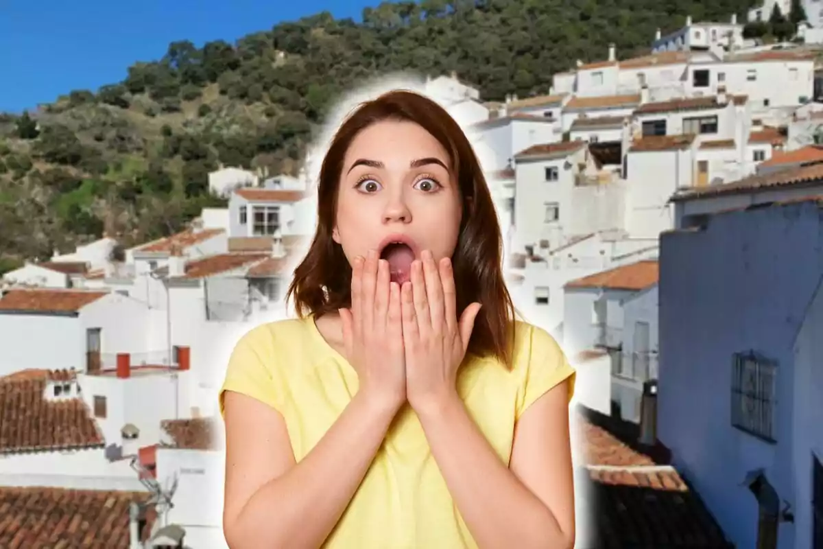 Mujer sorprendida con las manos en la boca frente a un paisaje de casas blancas con techos de tejas y colinas verdes.