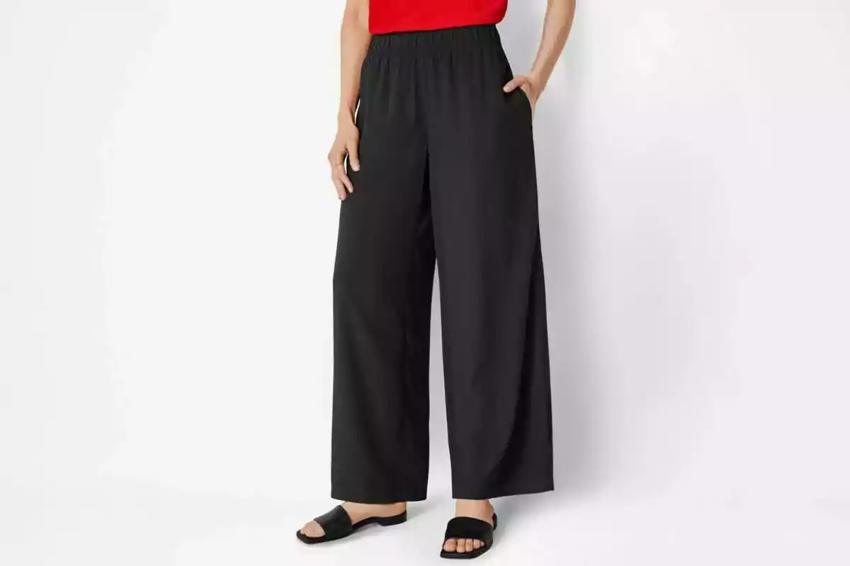 Persona vistiendo un pantalón negro de pierna ancha de Lidl con una blusa roja y sandalias negras. Persona vistiendo un pantalón negro de pierna ancha de Lidl con una blusa roja y sandalias negras.