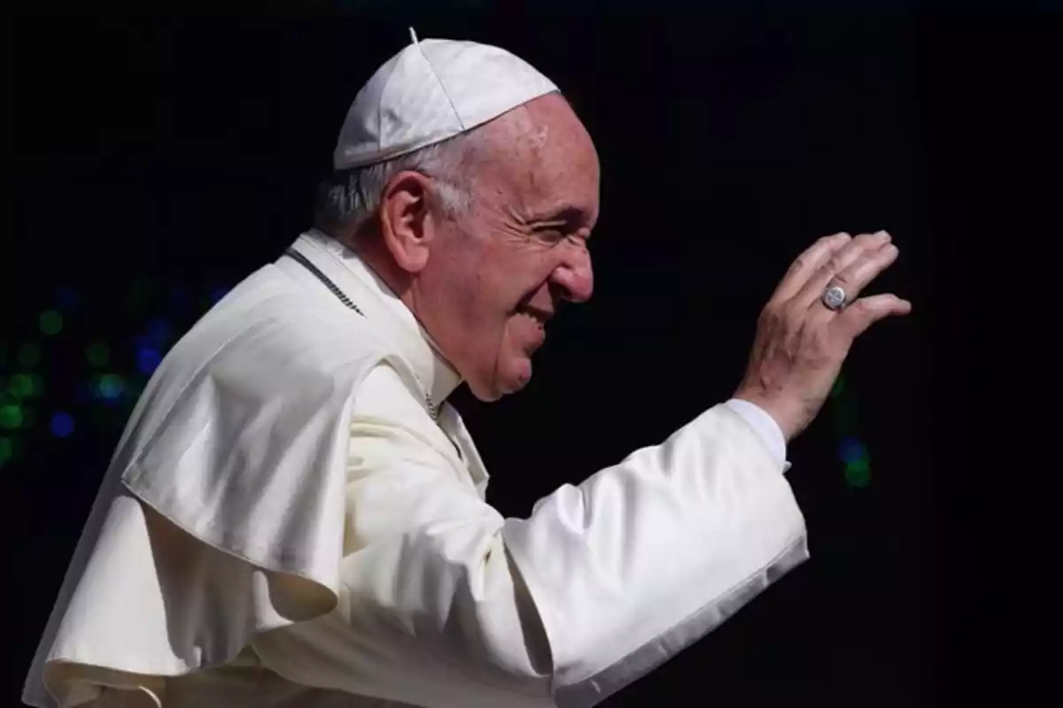 Un líder religioso vestido de blanco saluda con la mano.