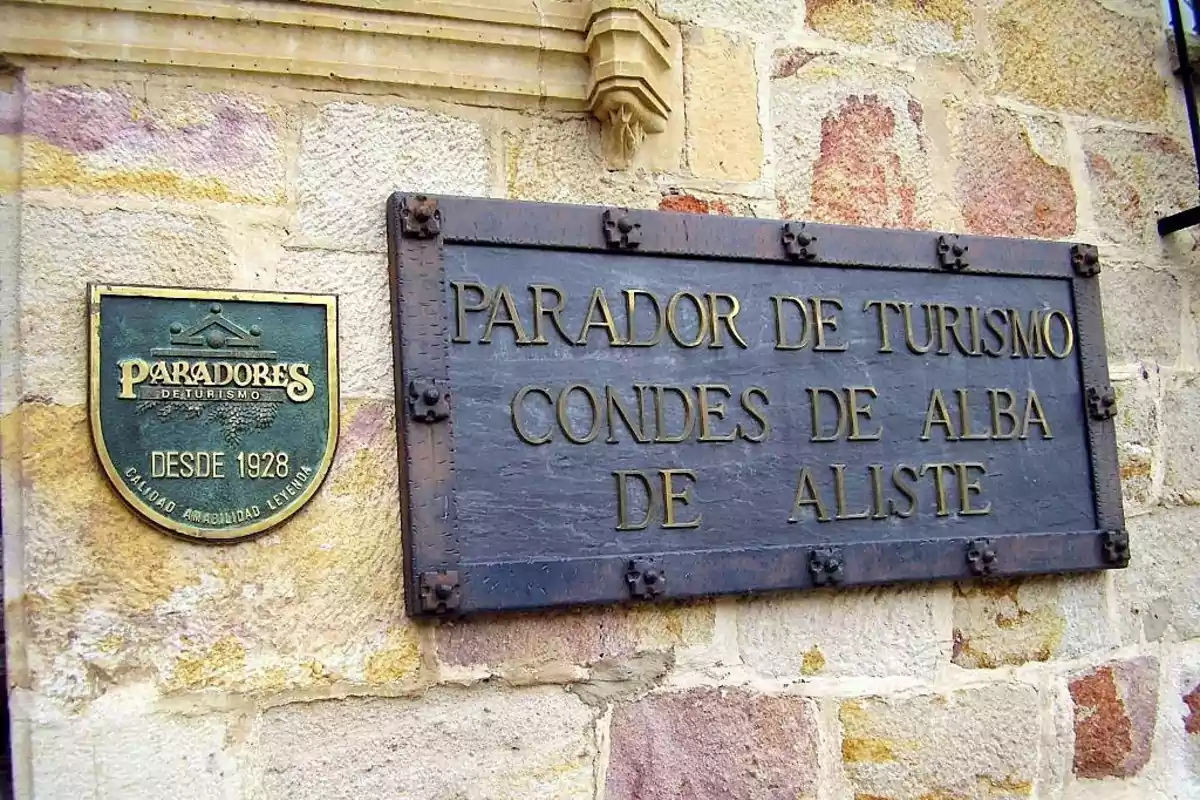 Placas de metal en una pared de piedra que indican "Parador de Turismo Condes de Alba de Aliste" y "Paradores de Turismo Desde 1928 Calidad Amabilidad Leyenda".