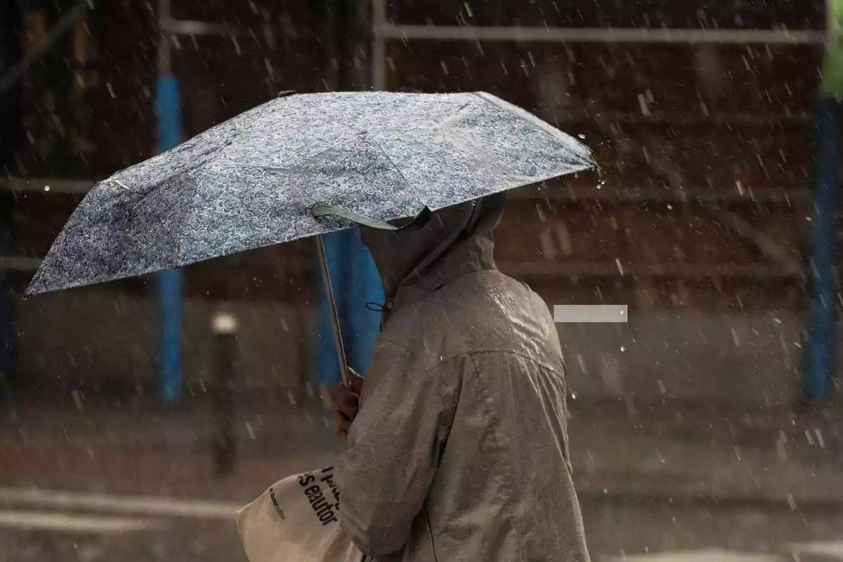 Mujer con un paraguas en la calle en medio de un temporal de lluvia Mujer con un paraguas en la calle en medio de un temporal de lluvia