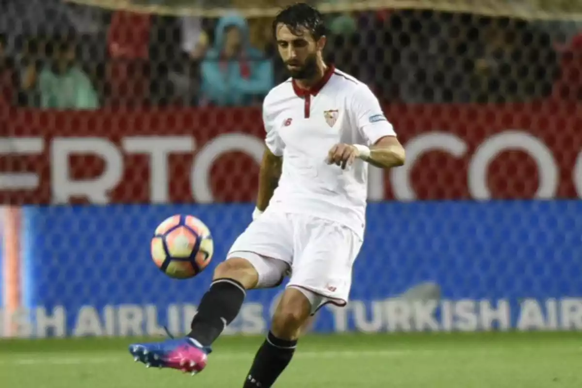 Futbolista con uniforme blanco controlando un balón durante un partido en un estadio Futbolista con uniforme blanco controlando un balón durante un partido en un estadio