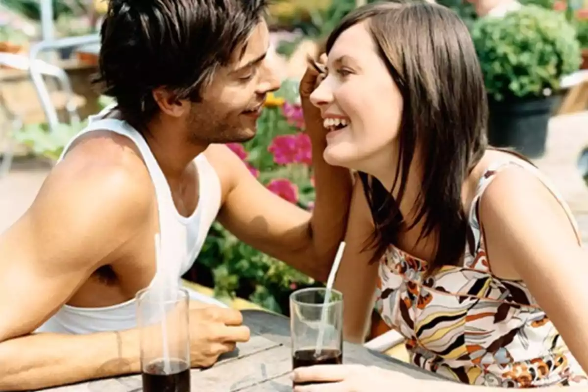 Una pareja sonriente disfrutando de una bebida en un entorno al aire libre con flores.