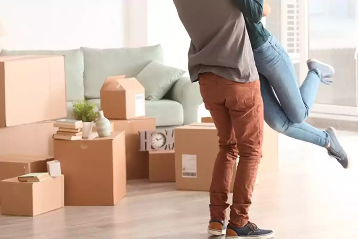 Pareja abrazándose en una sala llena de cajas de mudanza.