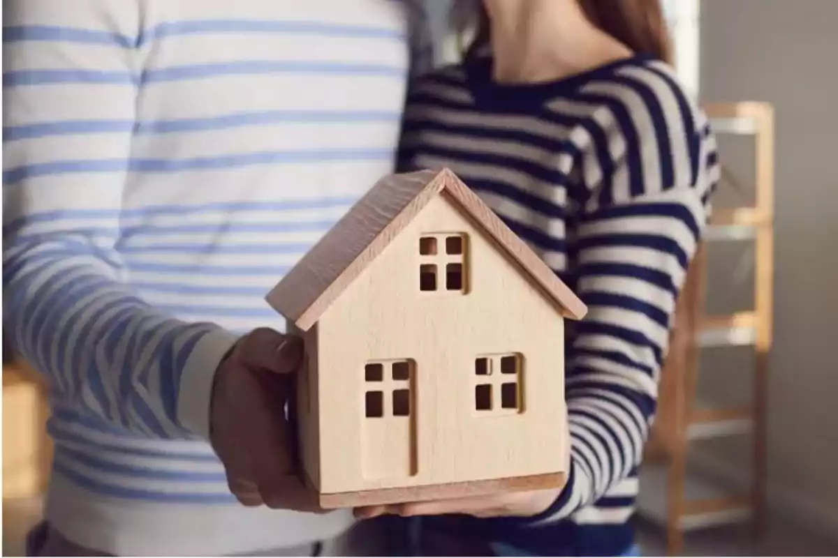 Una pareja sosteniendo una casa de madera en miniatura.