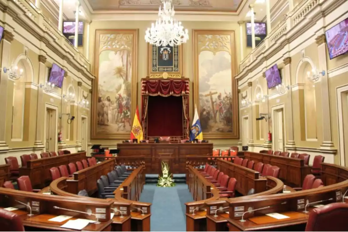 Una sala de asambleas con asientos de cuero rojo, un podio central con banderas y grandes pinturas en las paredes.