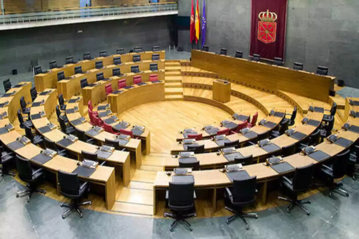 Vista del interior de un parlamento con asientos dispuestos en forma semicircular y una bandera en la pared.