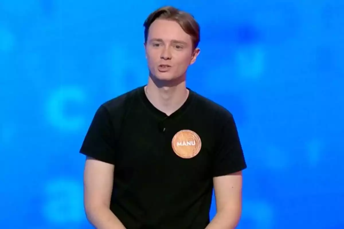 Manu con camiseta negra y una etiqueta que dice Manu sobre un fondo azul. Captura de 'Pasapalabra' Manu con camiseta negra y una etiqueta que dice Manu sobre un fondo azul. Captura de 'Pasapalabra'