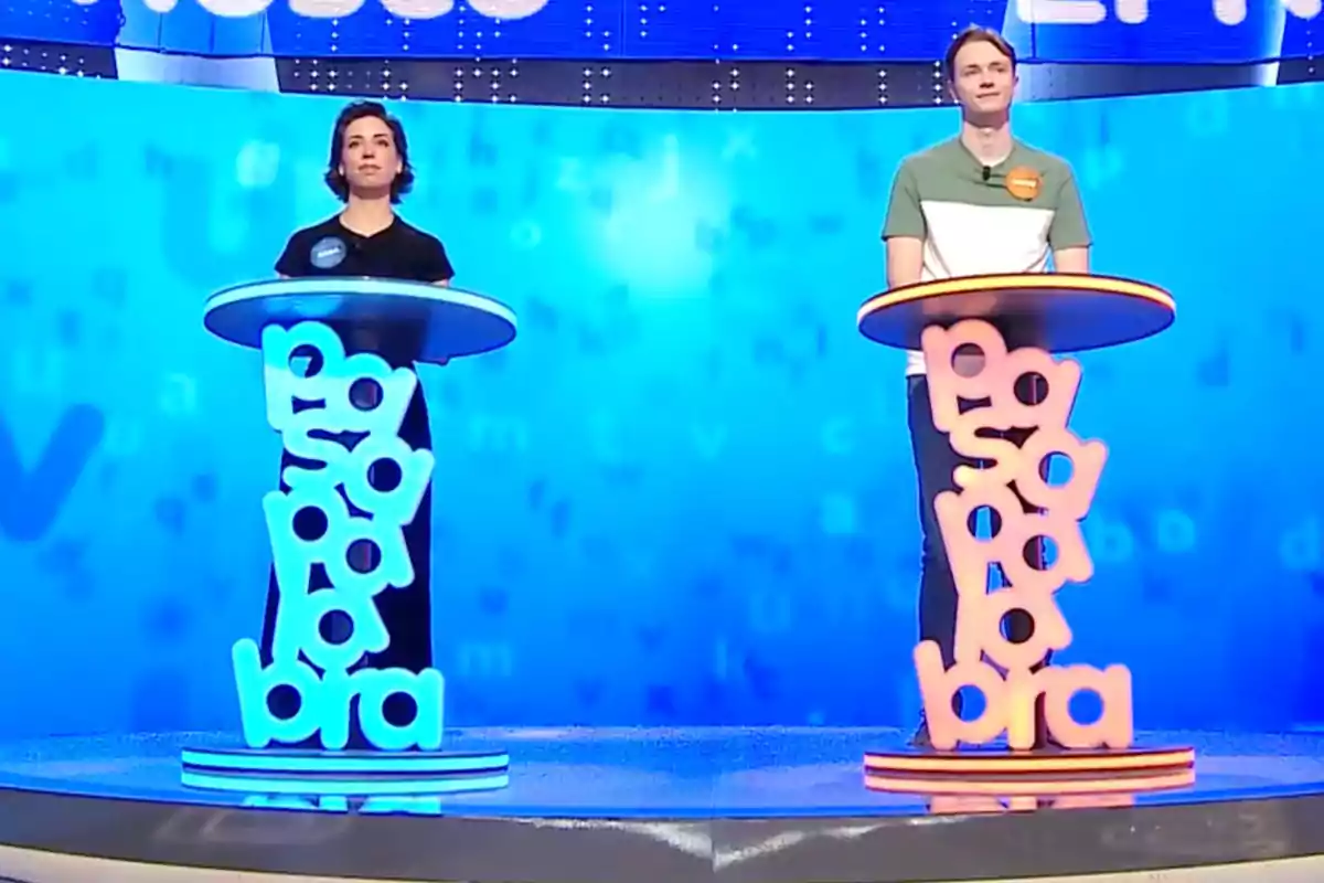 Manu y Rosa están de pie detrás de podios iluminados con las palabras Manu y Rosa están de pie detrás de podios iluminados con las palabras