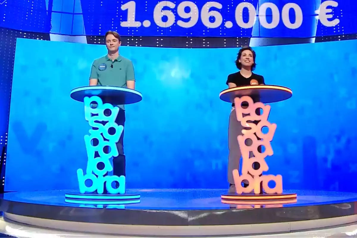 Manu y Rosa de pie en un plató de televisión junto a atriles iluminados con letras y una gran cifra de dinero en euros en la pantalla de fondo. Captura de 'Pasapalabra' Manu y Rosa de pie en un plató de televisión junto a atriles iluminados con letras y una gran cifra de dinero en euros en la pantalla de fondo. Captura de 'Pasapalabra'