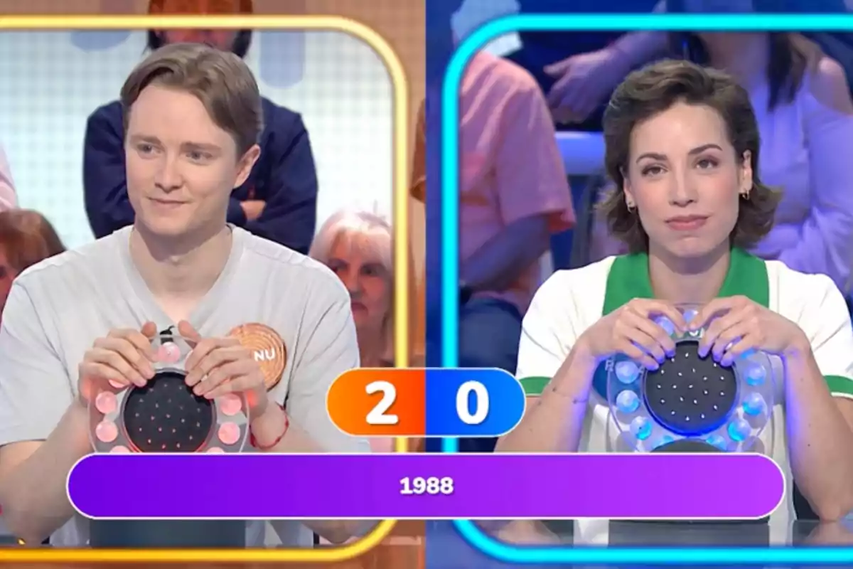 Manu y Rosa participan en un programa de televisión de preguntas y respuestas, cada uno sostiene un pulsador y el marcador muestra 2 a 0 con el año 1988 en la pantalla. Captura de 'Pasapalabra' Manu y Rosa participan en un programa de televisión de preguntas y respuestas, cada uno sostiene un pulsador y el marcador muestra 2 a 0 con el año 1988 en la pantalla. Captura de 'Pasapalabra'