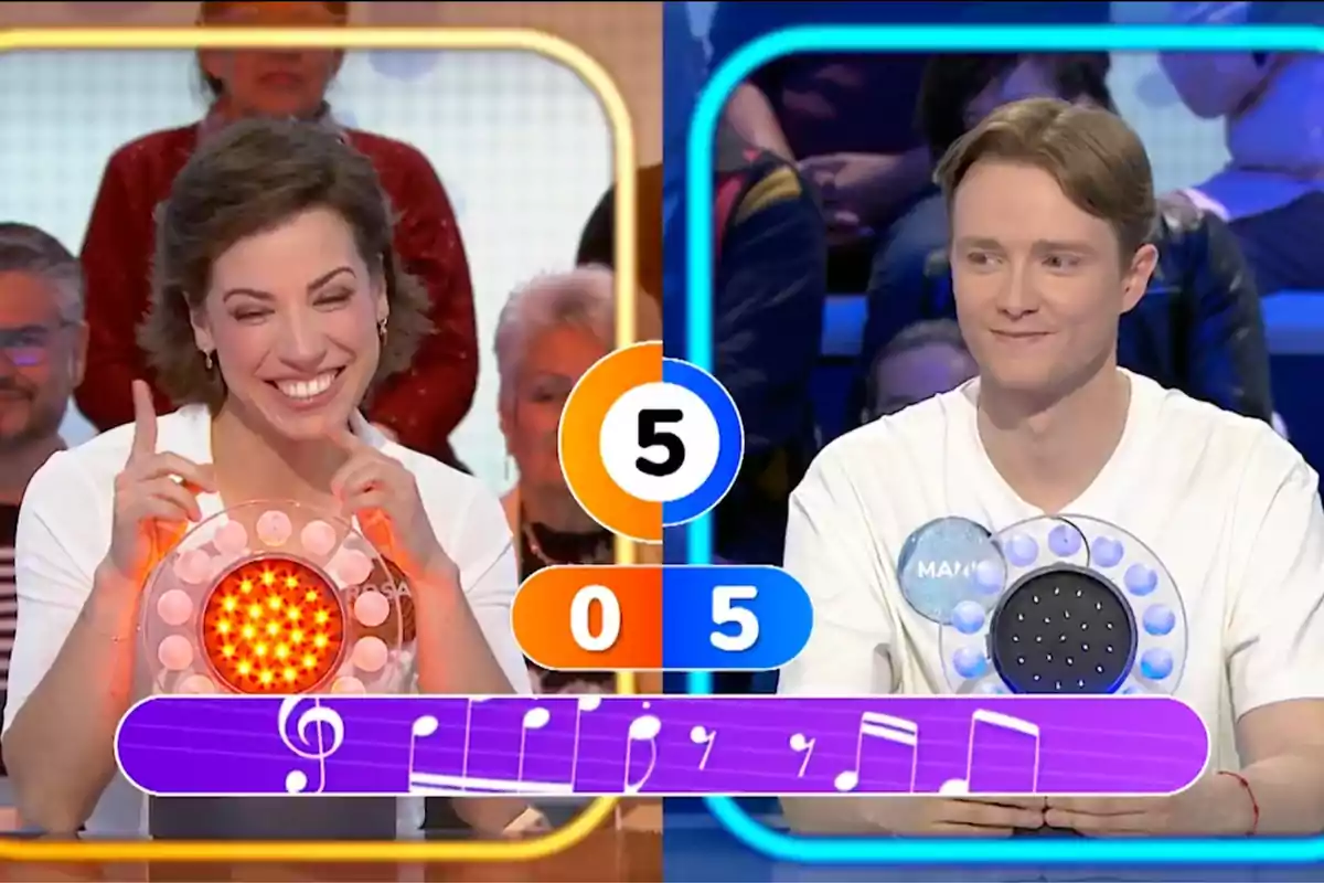 Rosa y Manu sonríen en un programa de juegos de televisión, cada uno con un panel de luces frente a ellos, mientras el marcador central muestra un puntaje de cinco a cero y una partitura musical aparece en la parte inferior de la imagen. Captura de 'Pasapalabra' Rosa y Manu sonríen en un programa de juegos de televisión, cada uno con un panel de luces frente a ellos, mientras el marcador central muestra un puntaje de cinco a cero y una partitura musical aparece en la parte inferior de la imagen. Captura de 'Pasapalabra'
