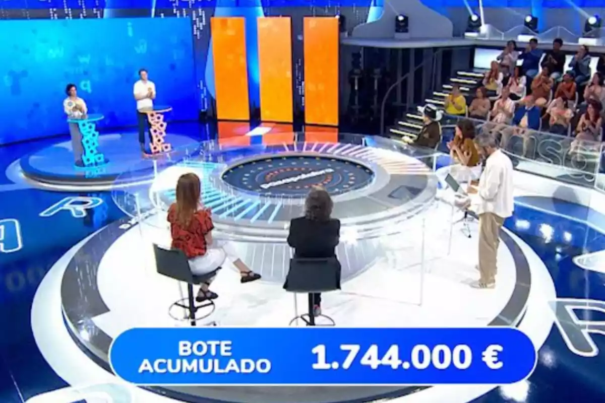 Un plató de concurso televisivo con concursantes, presentador, público y un marcador que muestra un bote acumulado de 1.744.000 euros. Captura de 'Pasapalabra' Un plató de concurso televisivo con concursantes, presentador, público y un marcador que muestra un bote acumulado de 1.744.000 euros. Captura de 'Pasapalabra'