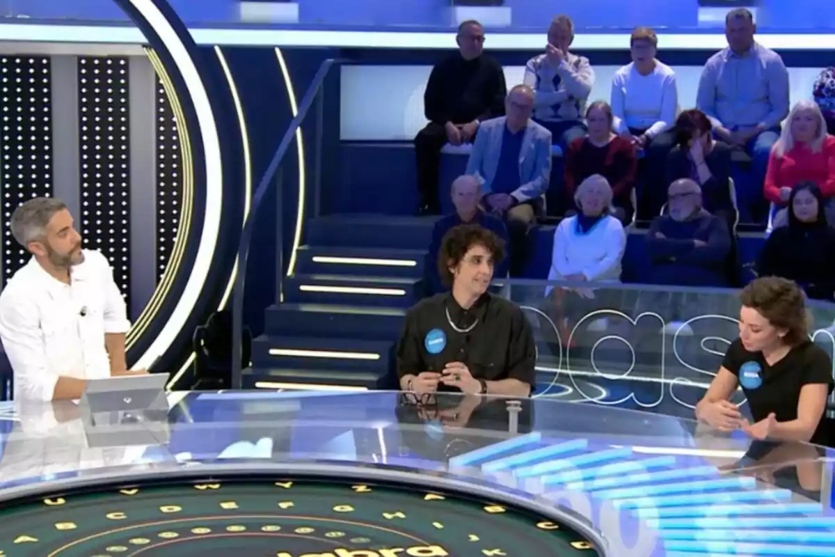 Roberto Leal interactúa con Canco Rodríguez y Rosa en un set de programa de juegos, mientras el público observa desde las gradas. Captura de 'Pasapalabra' Roberto Leal interactúa con Canco Rodríguez y Rosa en un set de programa de juegos, mientras el público observa desde las gradas. Captura de 'Pasapalabra'
