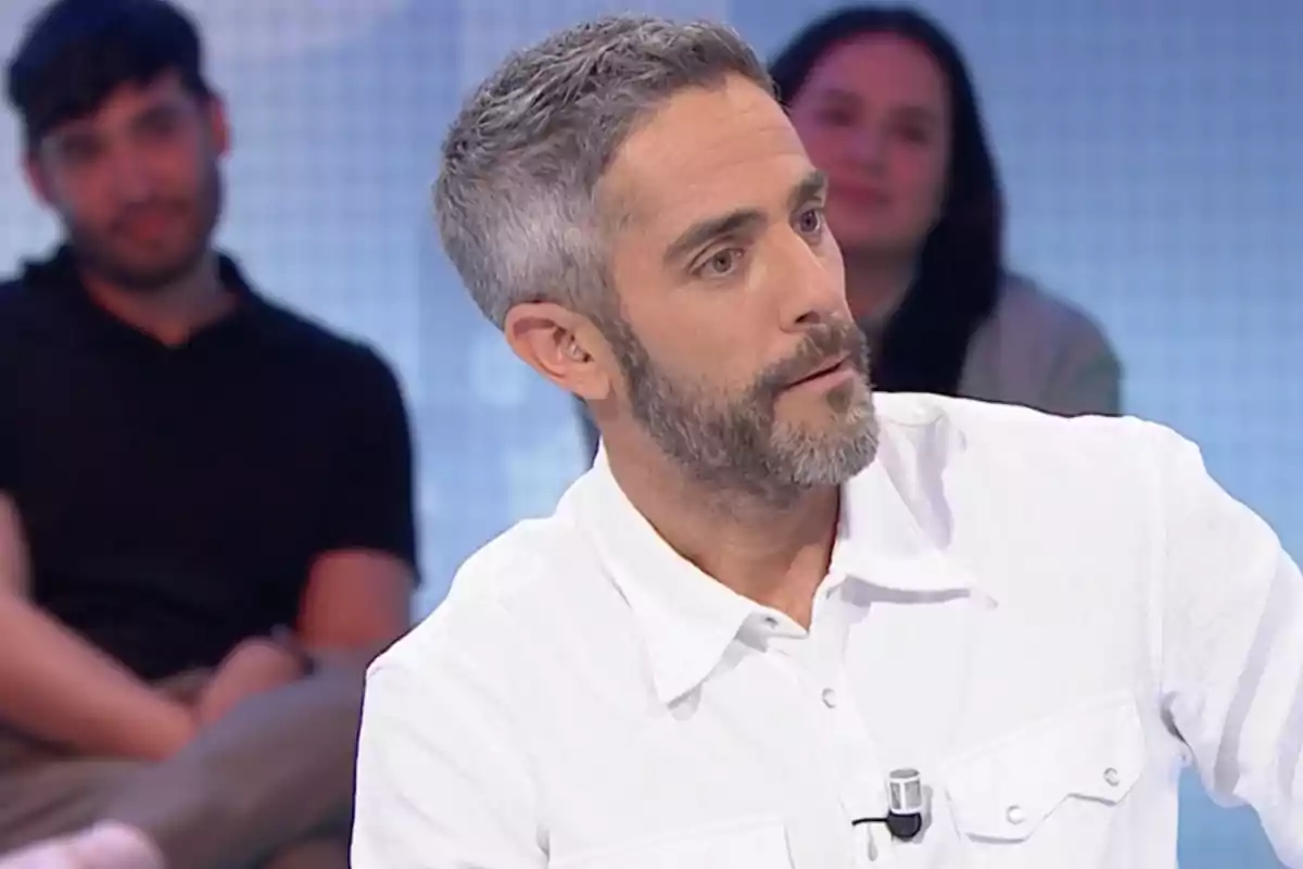 Roberto Leal está sentado en un estudio de televisión, vistiendo una camisa blanca, mientras dos personas están desenfocadas en el fondo. Captura de 'Pasapalabra' Roberto Leal está sentado en un estudio de televisión, vistiendo una camisa blanca, mientras dos personas están desenfocadas en el fondo. Captura de 'Pasapalabra'