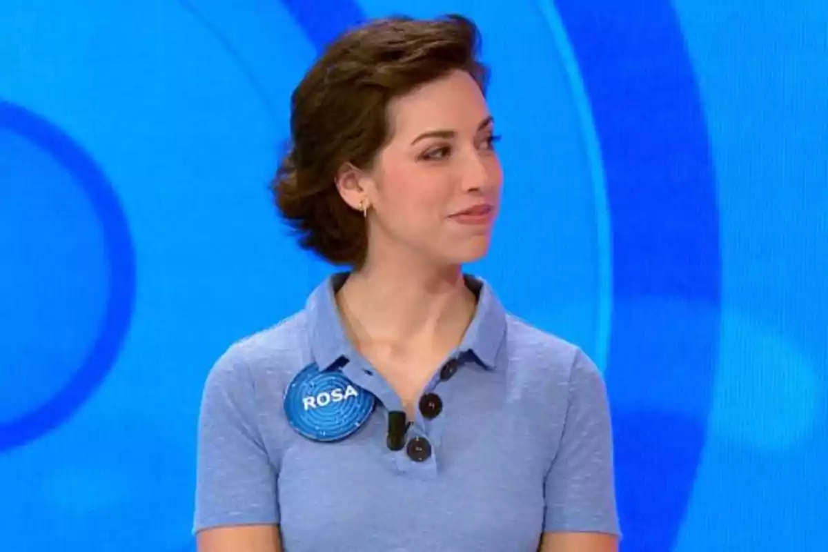 Rosa, lleva una camisa azul claro y una chapa con el nombre Rosa, está en un set de televisión con fondo azul. Captura de 'Pasapalabra' Rosa, lleva una camisa azul claro y una chapa con el nombre Rosa, está en un set de televisión con fondo azul. Captura de 'Pasapalabra'