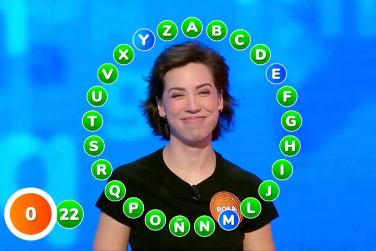 Rosa sonriente participando en un concurso de televisión con letras del abecedario rodeándola y un marcador de tiempo y aciertos en la esquina inferior izquierda. Captura de 'Pasapalabra' Rosa sonriente participando en un concurso de televisión con letras del abecedario rodeándola y un marcador de tiempo y aciertos en la esquina inferior izquierda. Captura de 'Pasapalabra'