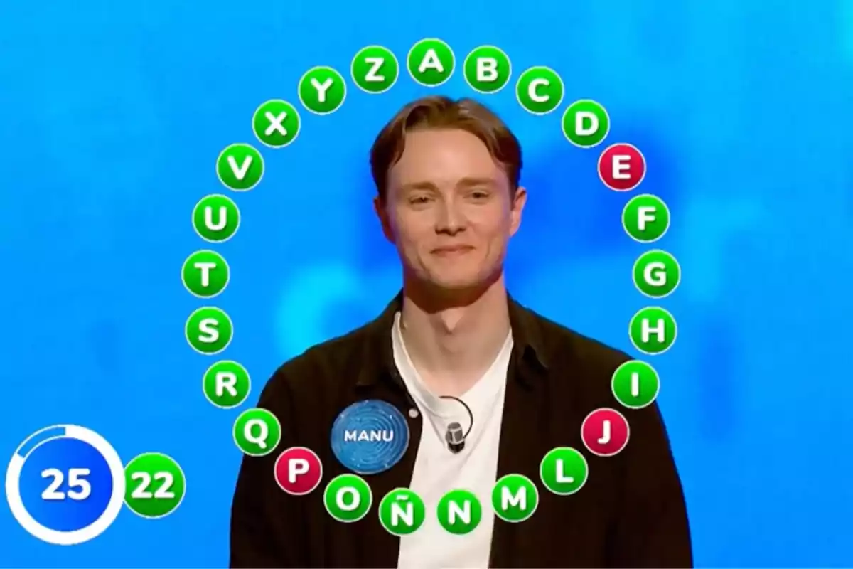 Manu en un programa de televisión está de pie frente a un fondo azul con un círculo de letras alrededor de su cabeza, algunas letras están en verde y otras en rojo, y hay un marcador de tiempo en la esquina inferior izquierda. Captura de 'Pasapalabra' Manu en un programa de televisión está de pie frente a un fondo azul con un círculo de letras alrededor de su cabeza, algunas letras están en verde y otras en rojo, y hay un marcador de tiempo en la esquina inferior izquierda. Captura de 'Pasapalabra'