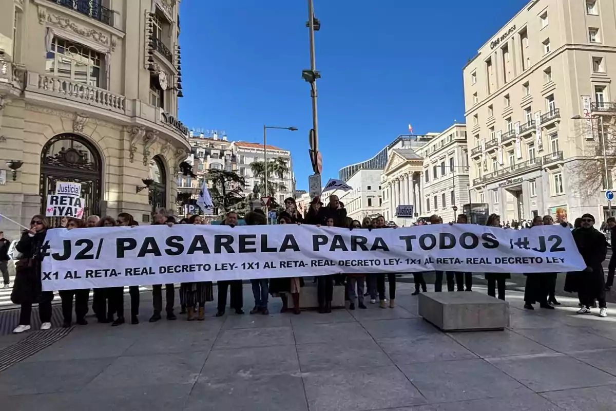 Un grupo de personas sostiene una pancarta en una manifestación en una calle de la ciudad, con edificios históricos de fondo.