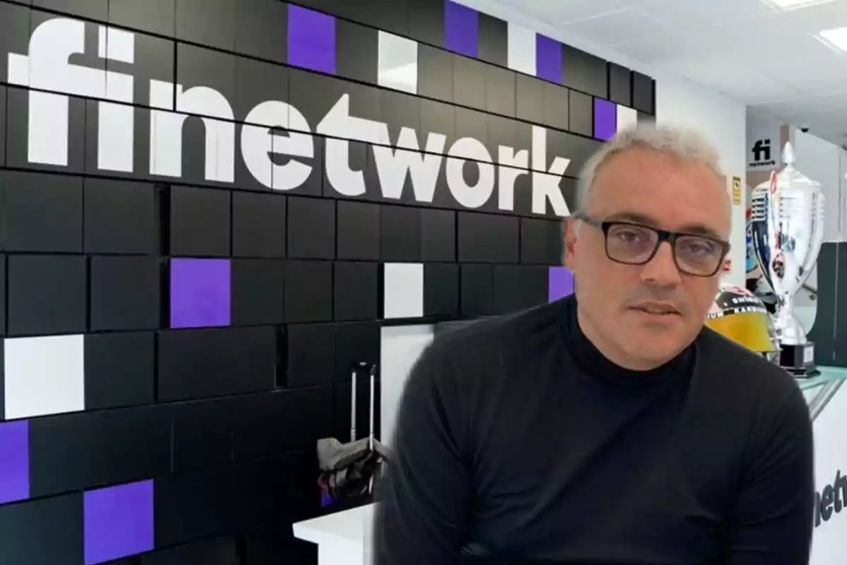 Un hombre con gafas y suéter negro está frente a una pared con el logo de "finetwork" en un entorno de oficina moderna.