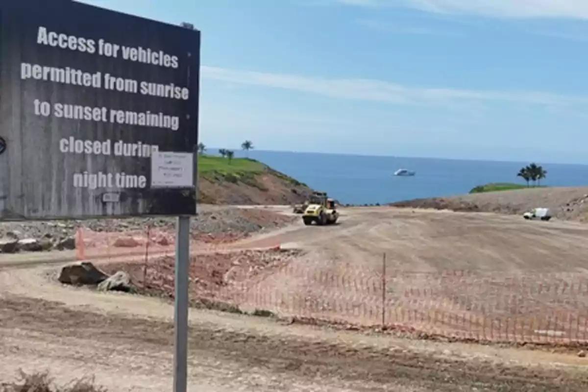Cartel de acceso para vehículos junto a una zona en construcción cerca del mar con maquinaria y una vista de un barco en el agua Cartel de acceso para vehículos junto a una zona en construcción cerca del mar con maquinaria y una vista de un barco en el agua
