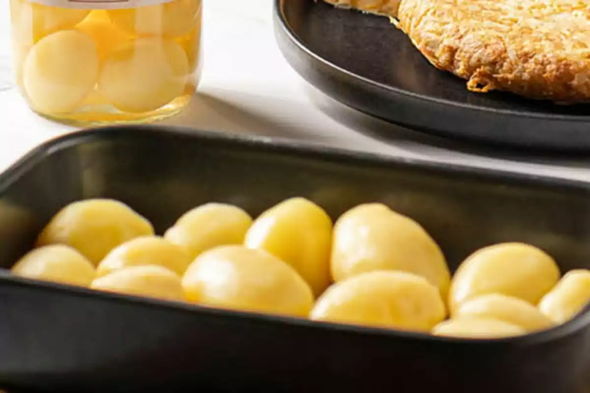 Un plato de patatas cocidas junto a un frasco de patatas en conserva y una tortilla en un plato negro. Un plato de patatas cocidas junto a un frasco de patatas en conserva y una tortilla en un plato negro.