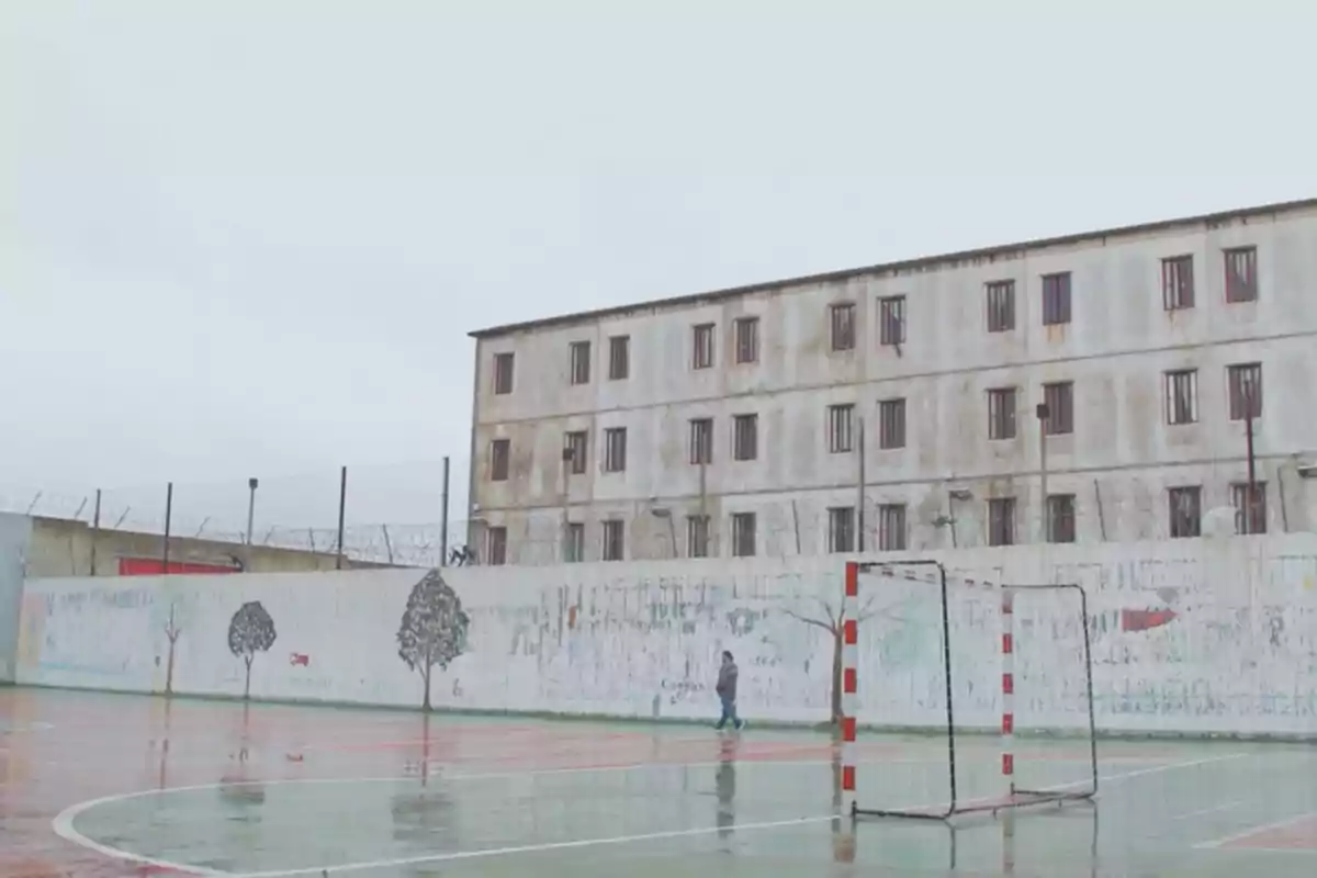 Una cancha de fútbol en un patio de una prisión con un edificio de varios pisos y ventanas con barrotes en el fondo.
