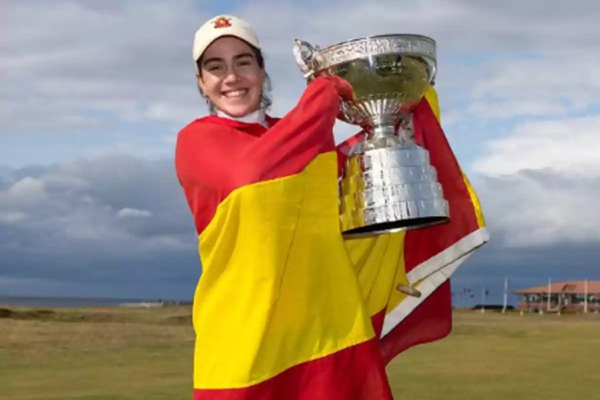 Joven sonriente envuelta en una bandera de España sostiene un gran trofeo plateado en un campo al aire libre
