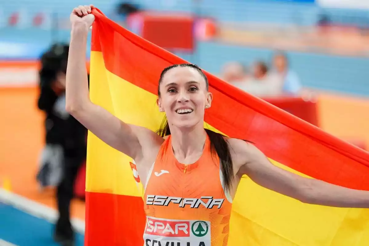Atleta sonriente sosteniendo la bandera de España en una pista cubierta. Atleta sonriente sosteniendo la bandera de España en una pista cubierta.