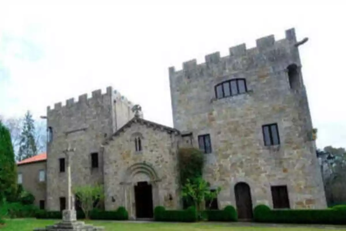 Edificio de piedra con torres y una entrada arqueada rodeado de vegetación.