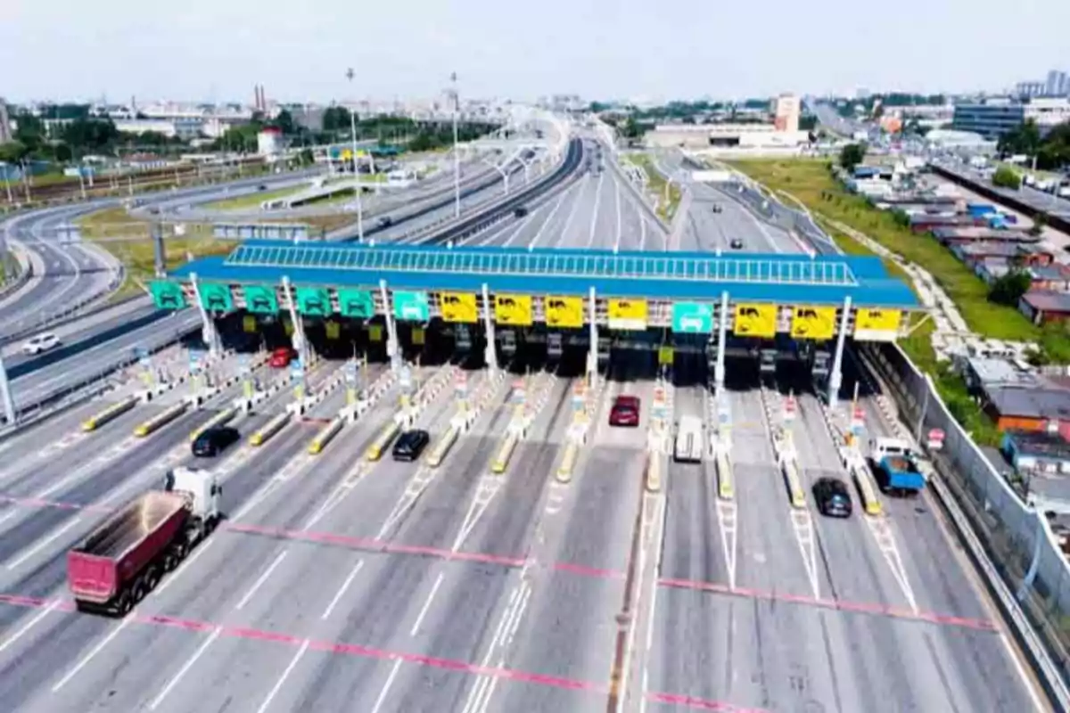 Vista aérea de una autopista con un peaje de varios carriles y vehículos pasando por las cabinas de pago.