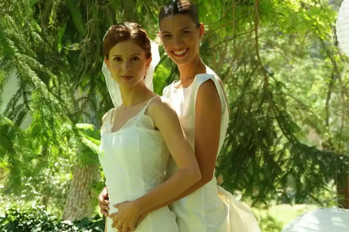 Dos mujeres vestidas de novia posan juntas en un entorno natural con árboles y vegetación.