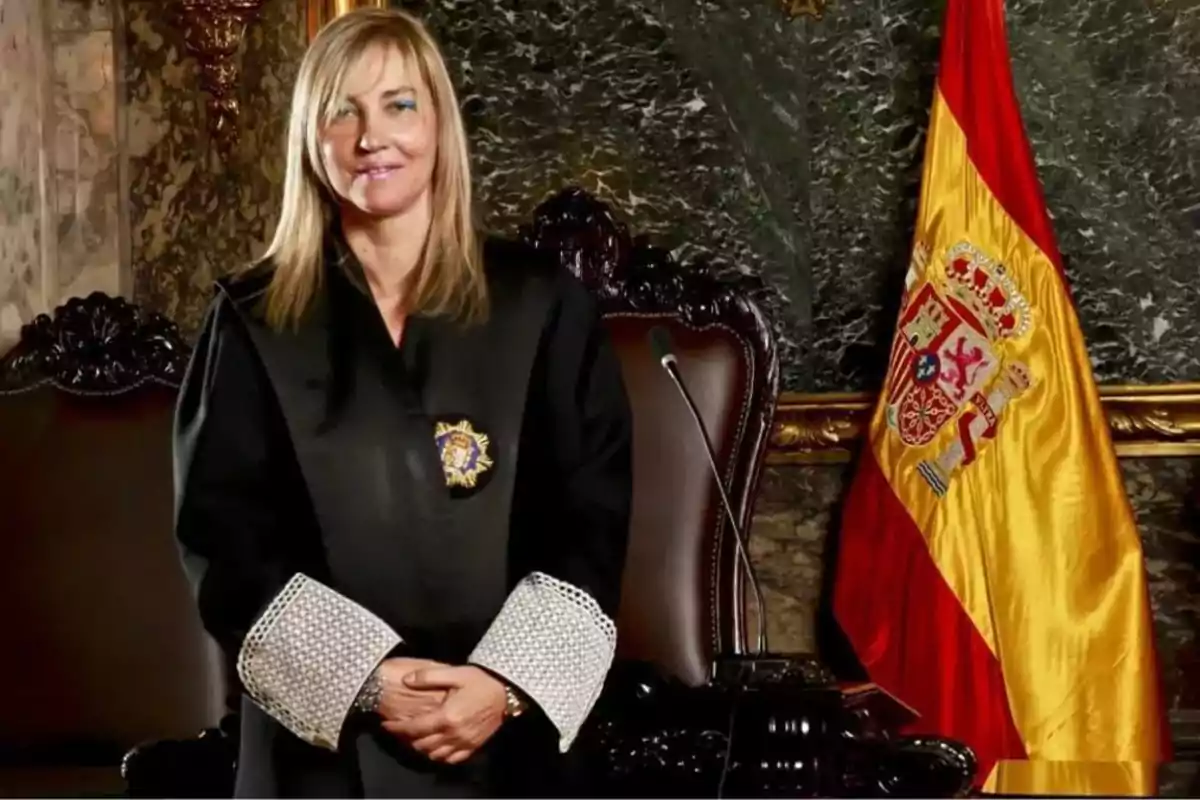 Una mujer con toga judicial posando frente a una bandera de España en un entorno formal.