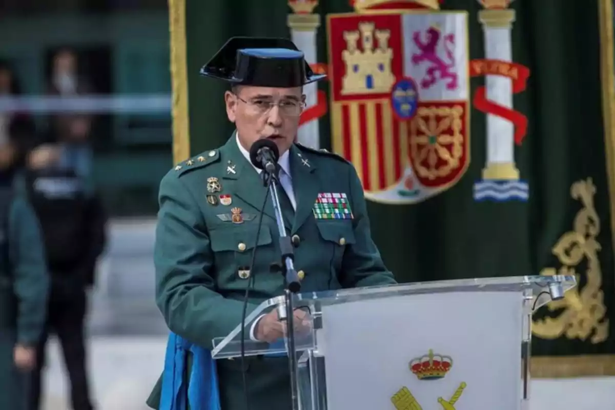 Un oficial de la Guardia Civil en uniforme formal habla en un podio con un escudo de España de fondo.