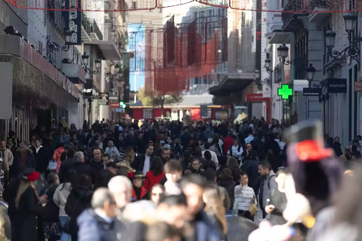 Una calle concurrida llena de personas caminando entre edificios con decoraciones colgantes y letreros de tiendas.