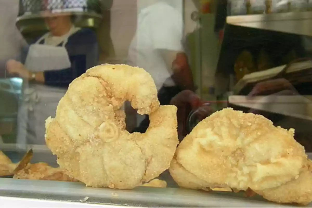 Dos piezas de pescado frito empanizado en una vitrina de exhibición con personas al fondo.