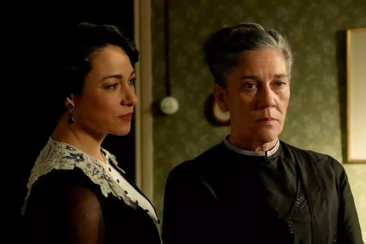 Isabel Serrano y Marga Martínez de pie en una habitación con expresión seria y vestimenta de época en La Promesa. Isabel Serrano y Marga Martínez de pie en una habitación con expresión seria y vestimenta de época en La Promesa.