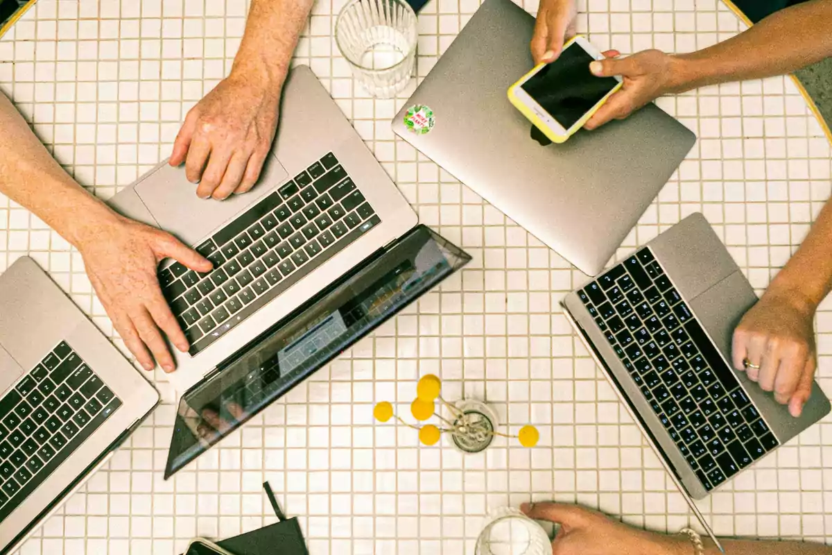 Personas trabajando en una mesa con computadoras portátiles y un teléfono móvil.