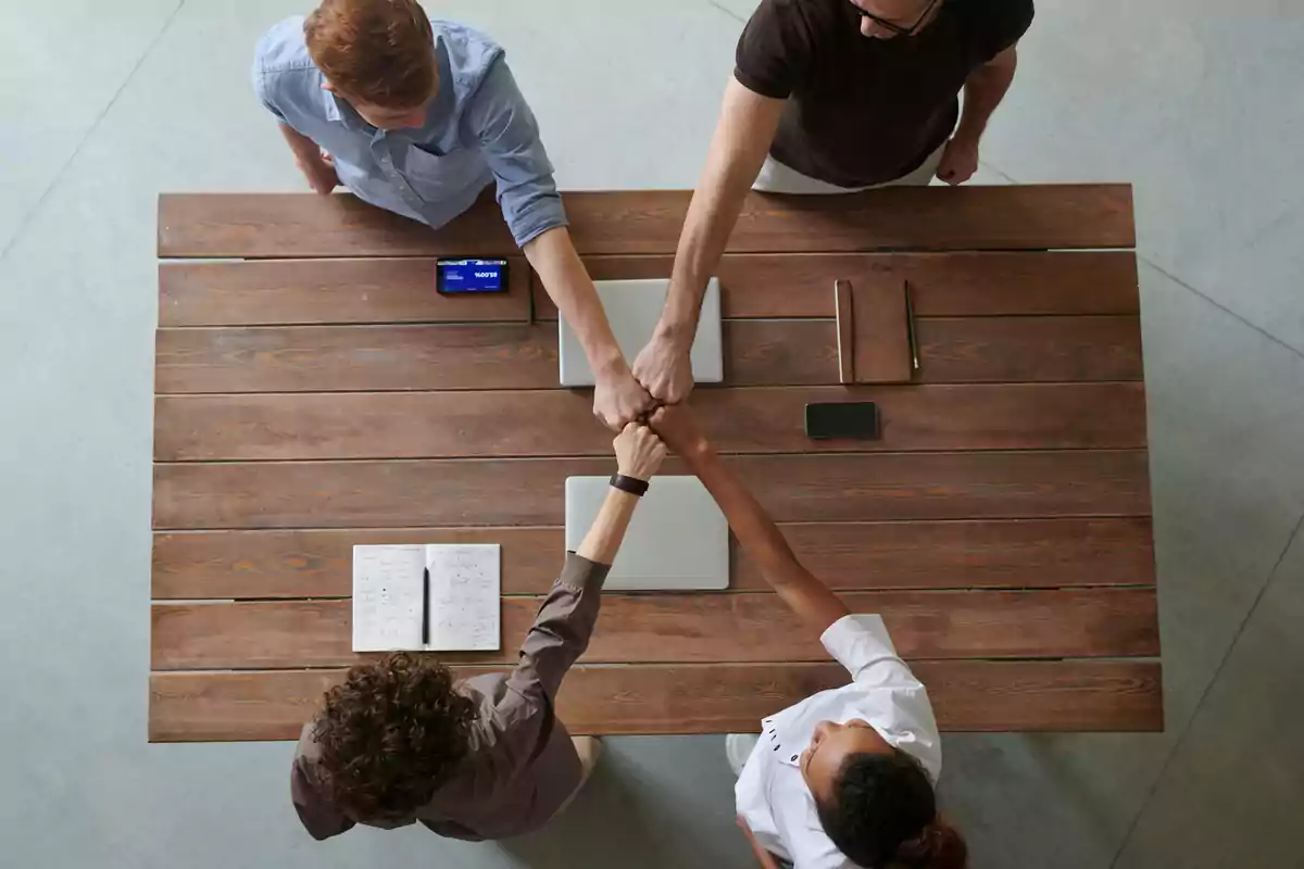 Cuatro personas se dan un puño en el centro de una mesa de madera durante una reunión de trabajo vista desde arriba